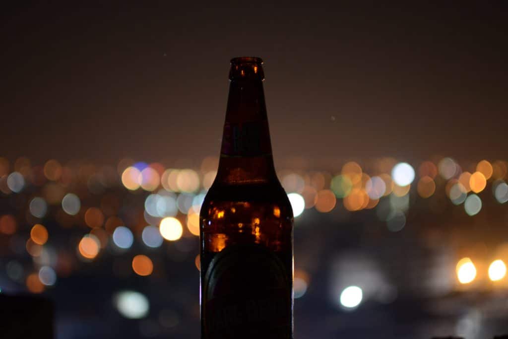 A bottle of beer in front of a city lights.