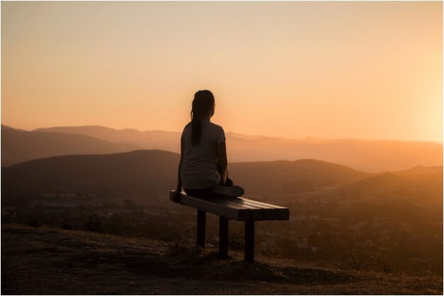 A woman sitting on a bench looking at the sunset.
