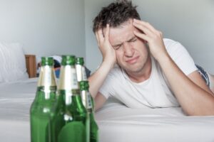 Man holds his head in pain while beer bottles are in the foreground