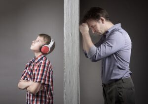 Depressed father leans his head on the wall while his teen son is on the other side wearing headphones