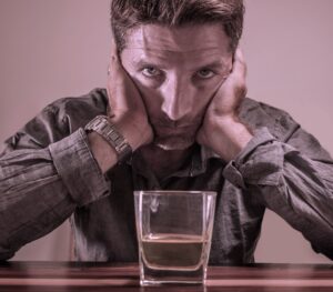 Man looking at a glass of whiskey asking himself how can I stay sober