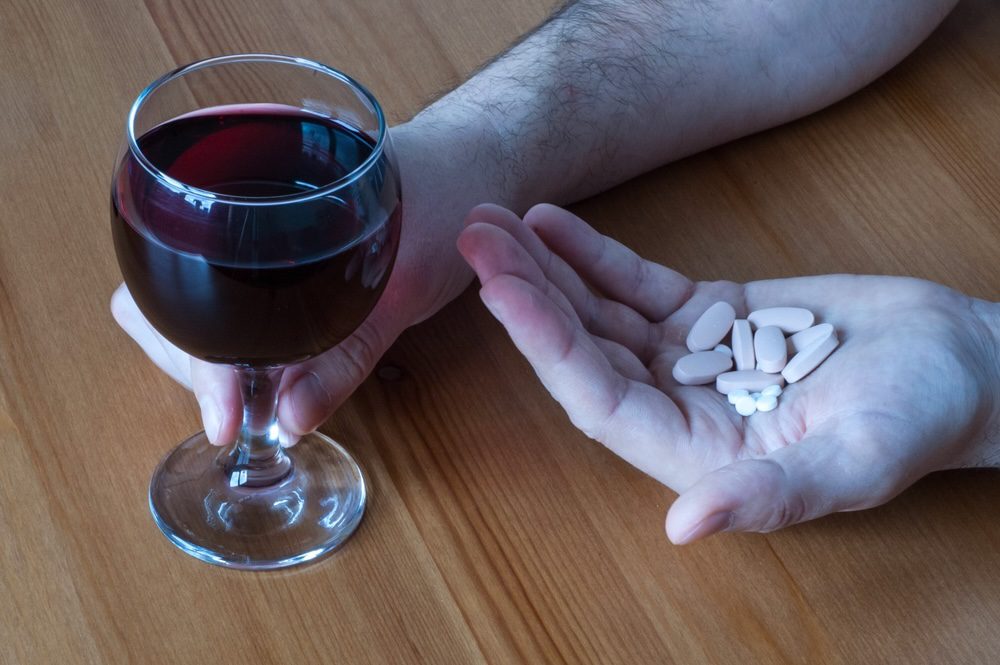 Hand holding trazodone pills with a glass of wine in the other hand