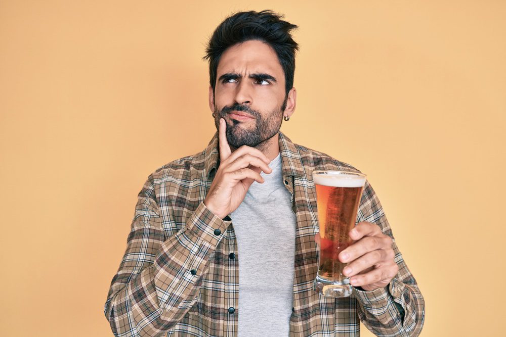 Man holding a glass of beer wondering how long alcohol stays in urine